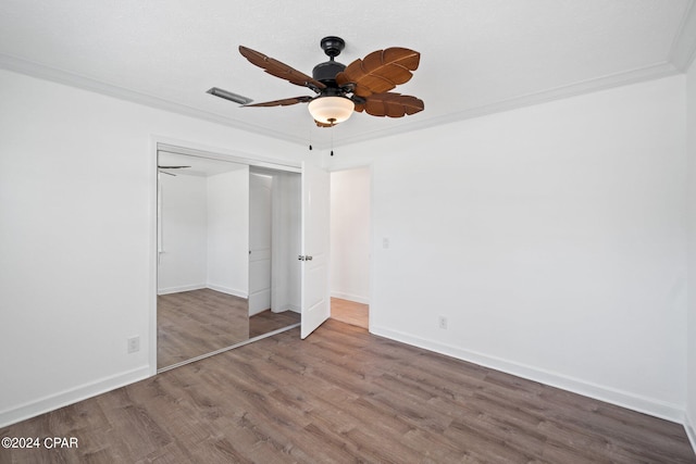 unfurnished bedroom featuring ceiling fan, crown molding, wood-type flooring, and a closet