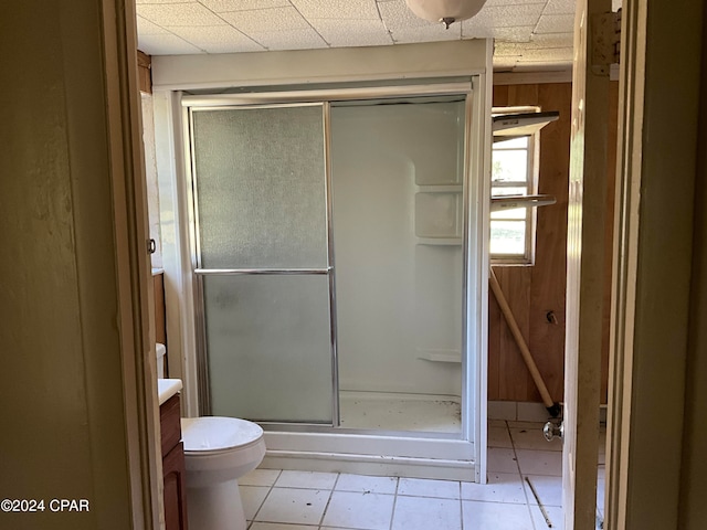 bathroom featuring a drop ceiling, tile patterned flooring, vanity, toilet, and a shower with door