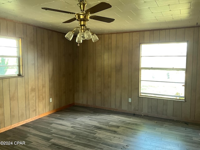 empty room with ceiling fan, wood-type flooring, and wood walls