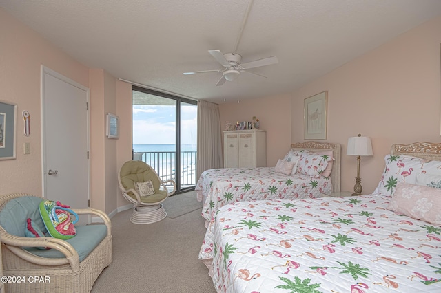 bedroom with a wall of windows, light colored carpet, access to exterior, a water view, and a textured ceiling