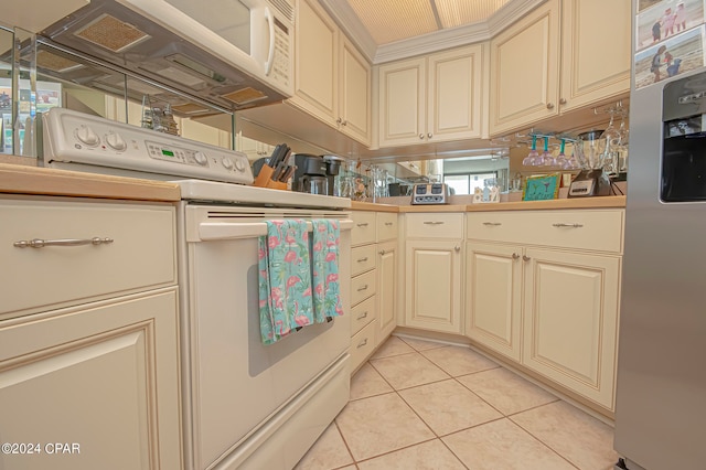 kitchen with white range oven, stainless steel fridge, light tile patterned floors, and cream cabinetry