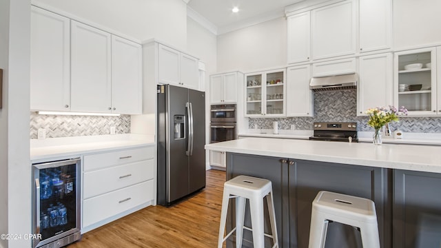 kitchen featuring a kitchen breakfast bar, white cabinetry, wine cooler, stainless steel appliances, and range hood