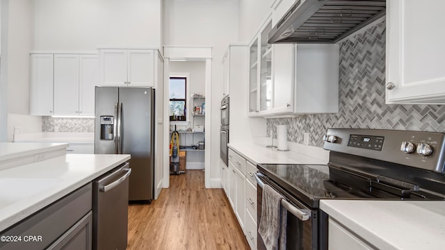 kitchen featuring light hardwood / wood-style floors, white cabinetry, wall chimney exhaust hood, backsplash, and appliances with stainless steel finishes