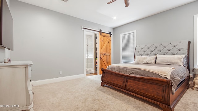 bedroom with ceiling fan, light colored carpet, ensuite bathroom, and a barn door