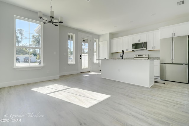 kitchen featuring stainless steel appliances, light stone countertops, an island with sink, and white cabinets