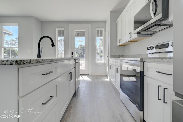 kitchen with appliances with stainless steel finishes, white cabinetry, sink, light stone counters, and light hardwood / wood-style flooring