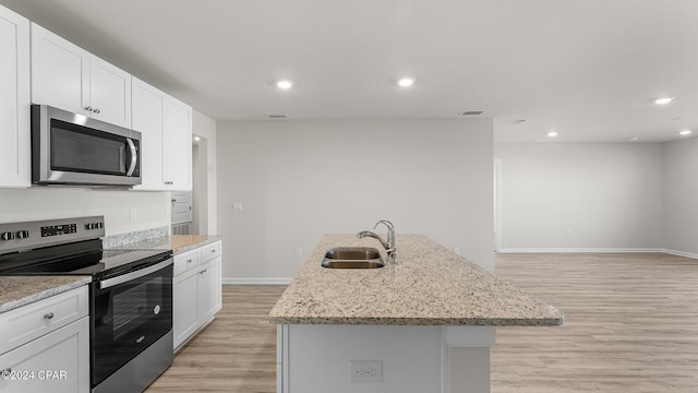 kitchen featuring sink, light wood-type flooring, an island with sink, appliances with stainless steel finishes, and white cabinetry