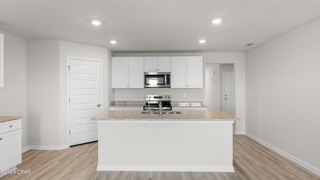 kitchen featuring white cabinets, an island with sink, stainless steel appliances, and light wood-type flooring