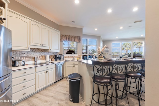 kitchen with backsplash, a kitchen breakfast bar, kitchen peninsula, appliances with stainless steel finishes, and white cabinets