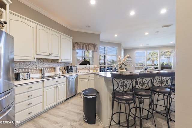 kitchen with a breakfast bar, stainless steel appliances, backsplash, ornamental molding, and a sink