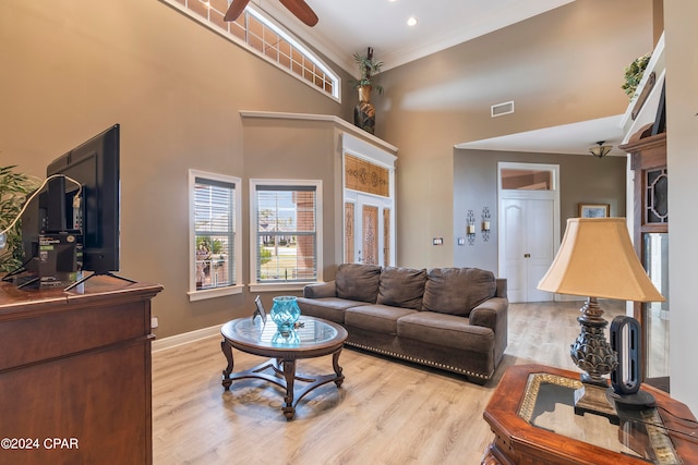 living room featuring ceiling fan, light hardwood / wood-style floors, crown molding, and a towering ceiling