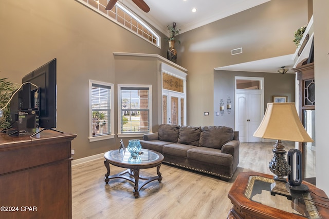 living area with a towering ceiling, visible vents, baseboards, ornamental molding, and light wood-type flooring