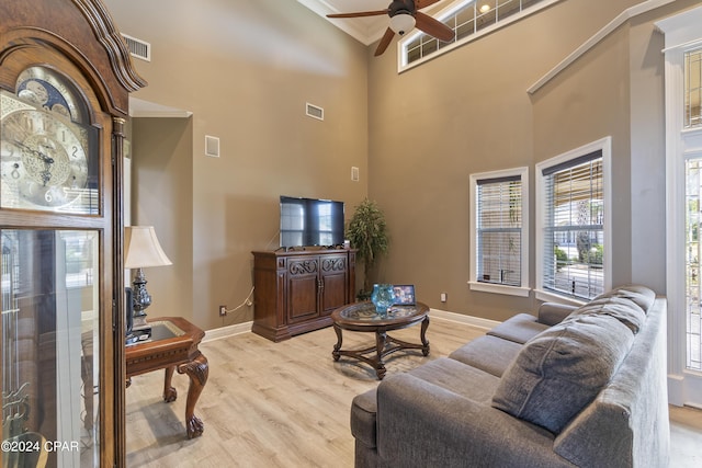 living area featuring baseboards, visible vents, light wood-style flooring, and a high ceiling