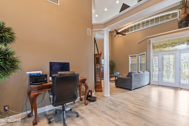 home office with a towering ceiling, decorative columns, and light hardwood / wood-style floors