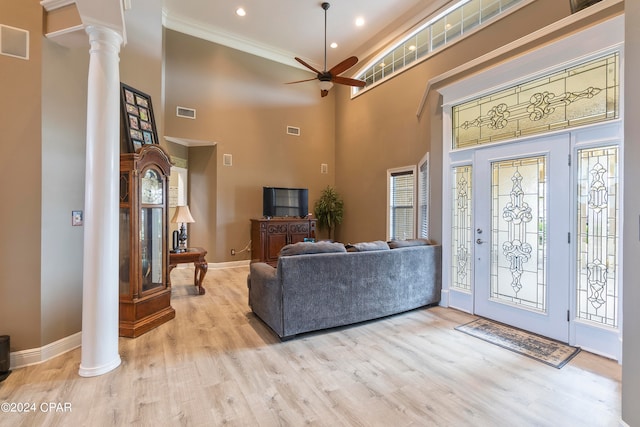 living room featuring a towering ceiling, light wood-type flooring, ceiling fan, and decorative columns