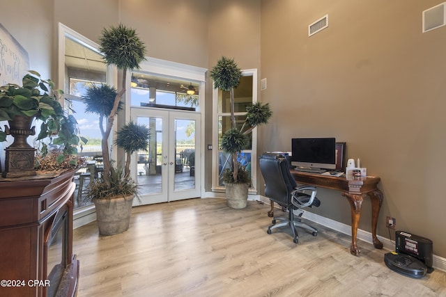 office featuring french doors, visible vents, a towering ceiling, and wood finished floors