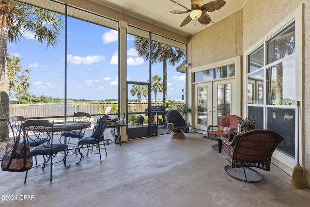 sunroom / solarium featuring a water view, plenty of natural light, a ceiling fan, and french doors