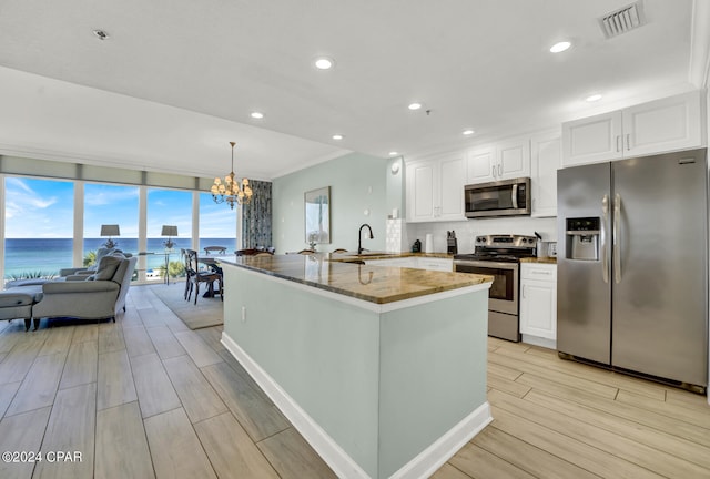 kitchen with stone countertops, a notable chandelier, stainless steel appliances, white cabinetry, and light wood-type flooring