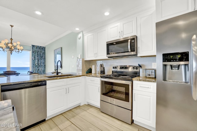 kitchen featuring white cabinets, an inviting chandelier, appliances with stainless steel finishes, light stone counters, and ornamental molding