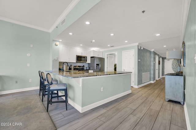 kitchen featuring light wood-type flooring, appliances with stainless steel finishes, white cabinetry, kitchen peninsula, and dark stone counters