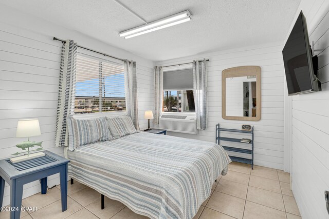 bedroom with cooling unit, wooden walls, a textured ceiling, and light tile patterned flooring