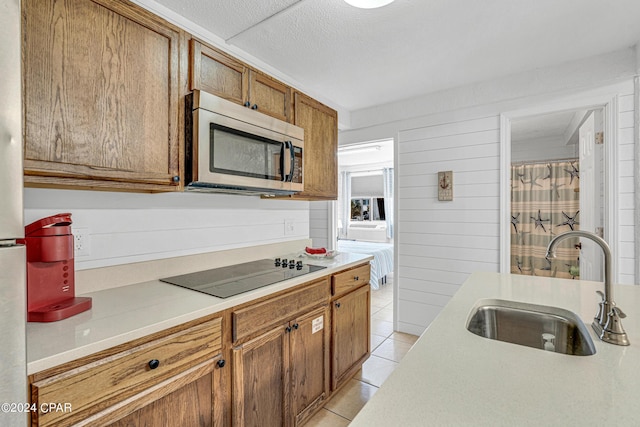 kitchen featuring light tile patterned floors, wooden walls, sink, and black electric stovetop