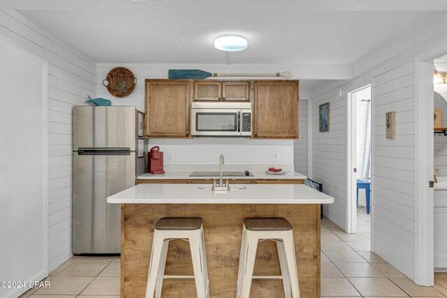 kitchen with a kitchen island with sink, appliances with stainless steel finishes, wooden walls, and a breakfast bar area