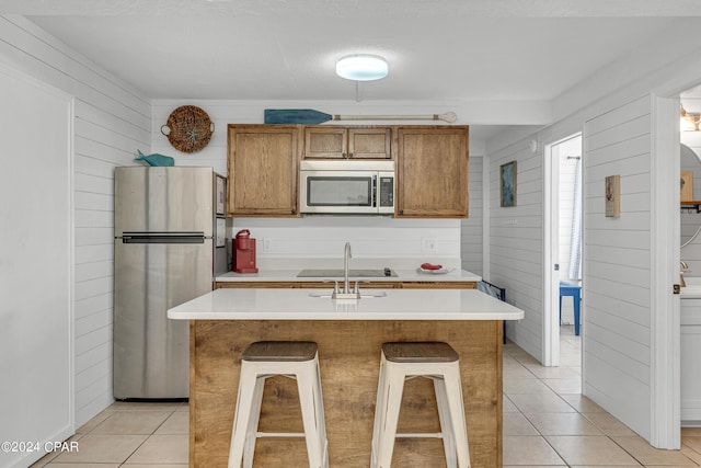 kitchen featuring light tile patterned flooring, light countertops, wood walls, brown cabinetry, and stainless steel appliances