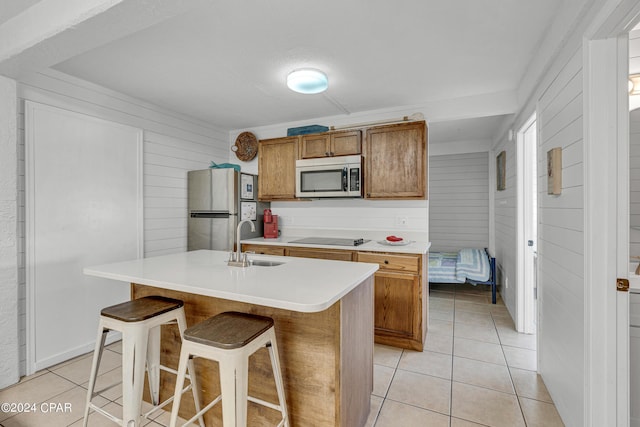 kitchen with wood walls, a center island with sink, a breakfast bar area, appliances with stainless steel finishes, and sink