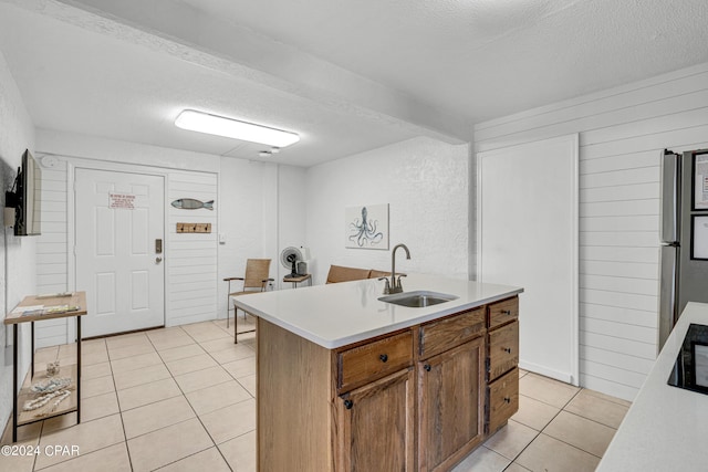 kitchen with a textured ceiling, light tile patterned floors, a center island with sink, and sink