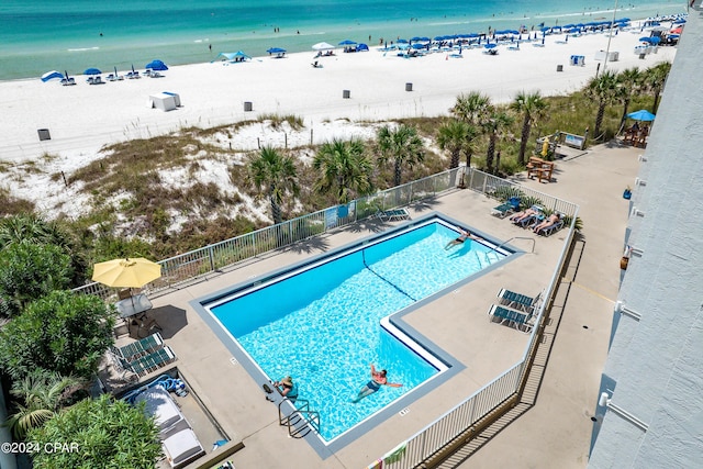 community pool with fence, a beach view, a water view, and a patio area