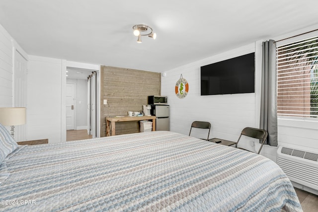 bedroom with stainless steel fridge, light hardwood / wood-style flooring, and a wall mounted air conditioner