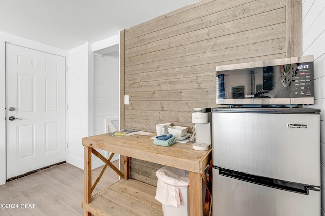 kitchen featuring stainless steel microwave, wood walls, and light wood-style flooring