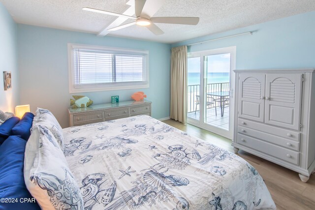 bedroom with a textured ceiling, light hardwood / wood-style floors, access to outside, ceiling fan, and a water view