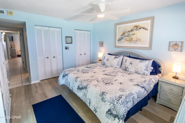 bedroom with a textured ceiling, ceiling fan, wood-type flooring, and multiple closets