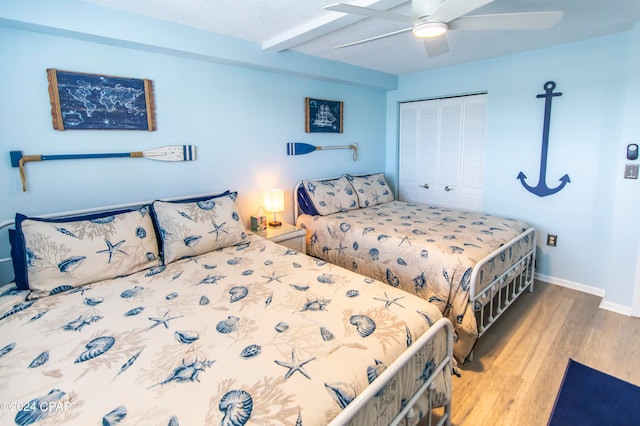 bedroom featuring light wood-type flooring, beamed ceiling, ceiling fan, and a closet