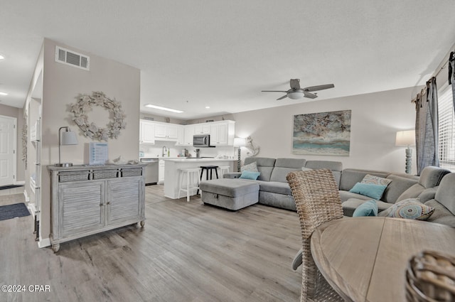 living room with a textured ceiling, light hardwood / wood-style floors, and ceiling fan