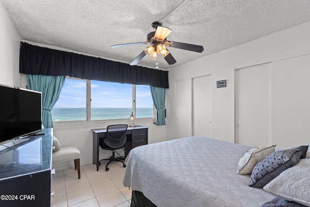 tiled bedroom featuring a water view, two closets, ceiling fan, and a textured ceiling