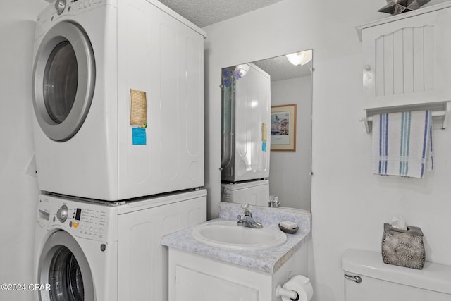 laundry area featuring stacked washer and dryer, sink, and a textured ceiling