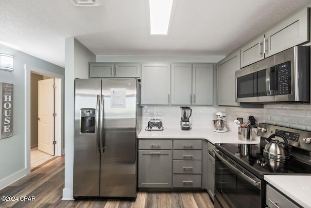 kitchen with dark wood-type flooring, gray cabinets, stainless steel appliances, and decorative backsplash