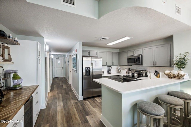 kitchen featuring stainless steel appliances, dark hardwood / wood-style flooring, kitchen peninsula, a breakfast bar, and gray cabinetry