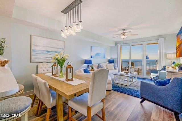 dining space with ceiling fan with notable chandelier, a water view, and hardwood / wood-style floors