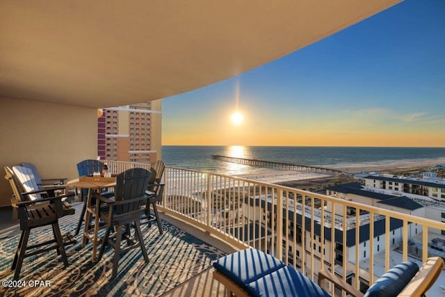 balcony at dusk featuring a view of the beach and a water view