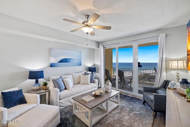 living room with a textured ceiling, dark wood-type flooring, ceiling fan, and a water view