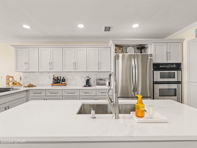 kitchen with a center island with sink, appliances with stainless steel finishes, tasteful backsplash, crown molding, and light stone counters