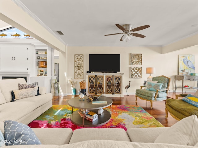 living room featuring hardwood / wood-style flooring, a fireplace, built in features, ceiling fan, and ornamental molding