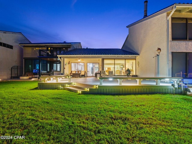 back house at dusk featuring a patio area and a yard