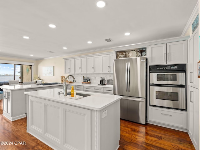 kitchen with an island with sink, kitchen peninsula, stainless steel appliances, and dark hardwood / wood-style floors