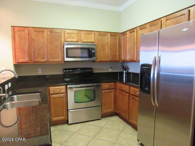 kitchen featuring appliances with stainless steel finishes, dark stone countertops, light tile patterned floors, crown molding, and sink