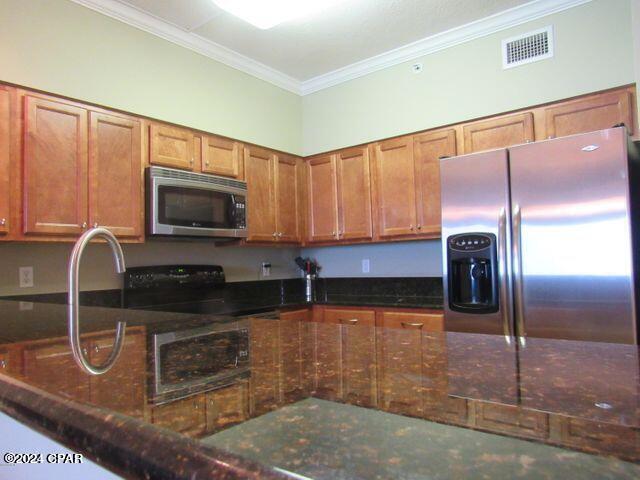 kitchen featuring stainless steel appliances, dark stone countertops, and crown molding